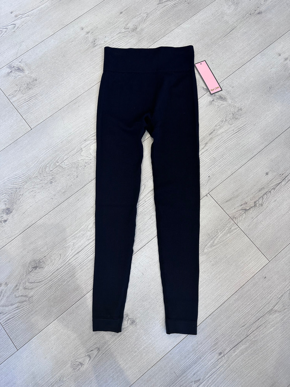 Black ribbed high-waist leggings for women displayed flat on light wooden floor, featuring a soft stretch fabric and seamless design