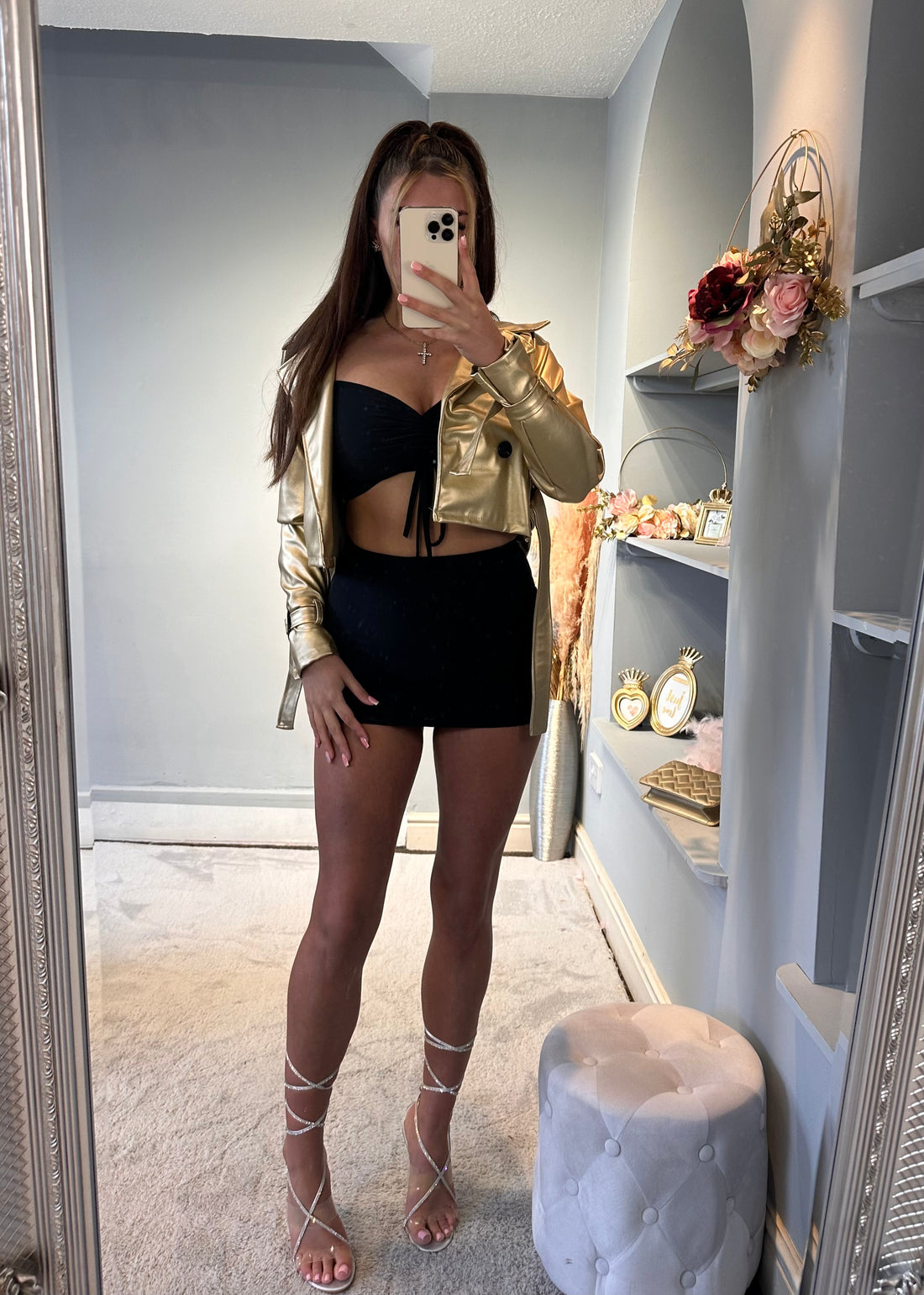 Stylish woman in gold metallic cropped jacket, black strapless mini dress, and rhinestone lace-up heels posing indoors — chic party or clubwear fashion outfit