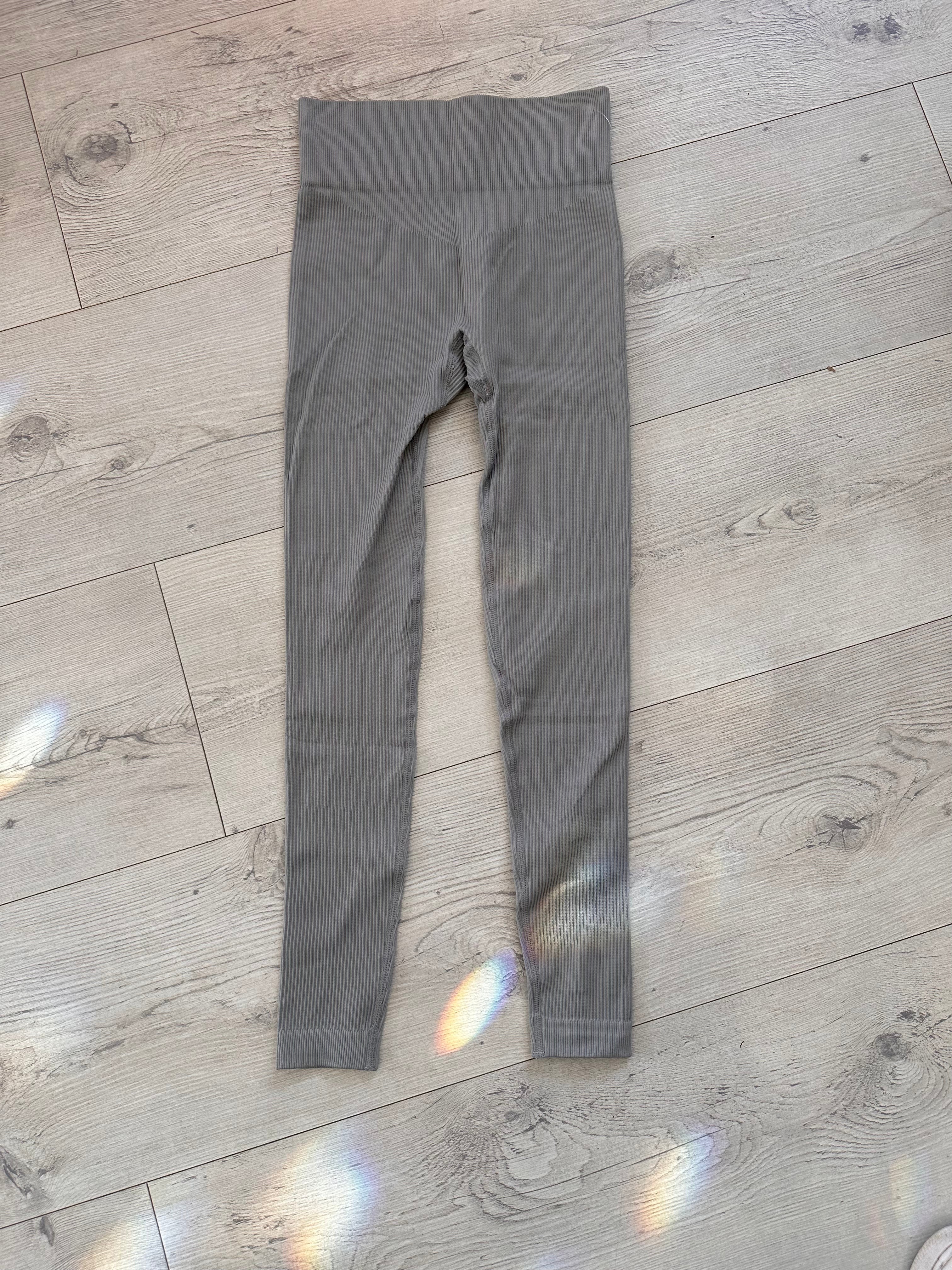 Flat lay of grey ribbed high-waisted leggings with V-shaped contour waistband, placed on a light wood floor with rainbow light reflections