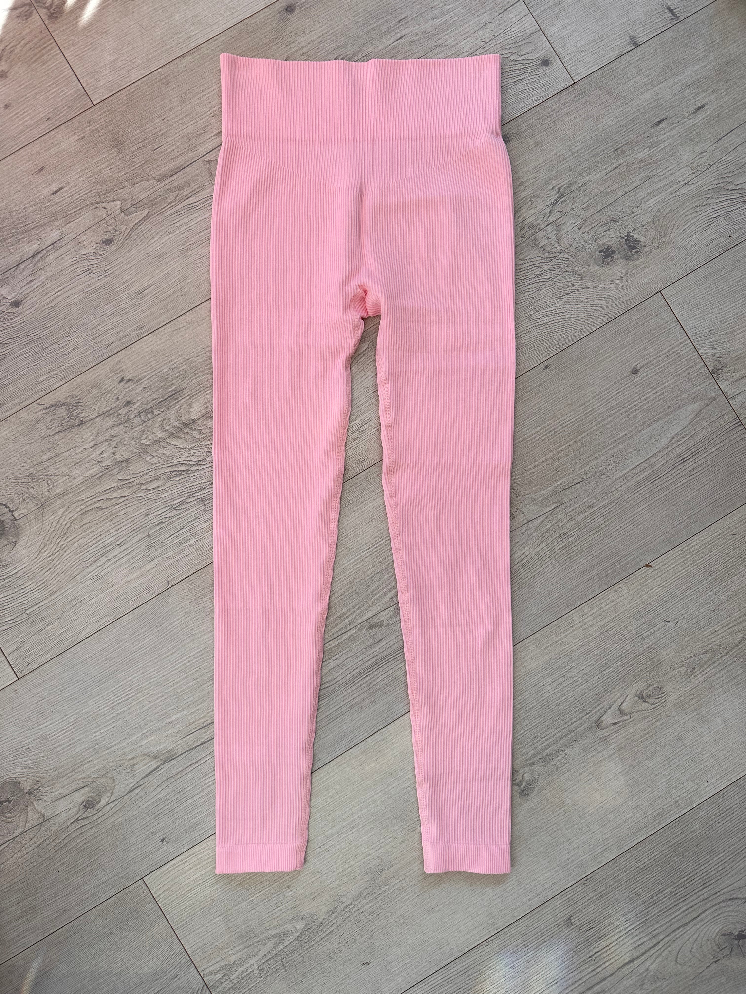 Flat lay of pink ribbed high-waisted leggings with a contour waistband, displayed on a light wood floor under natural sunlight