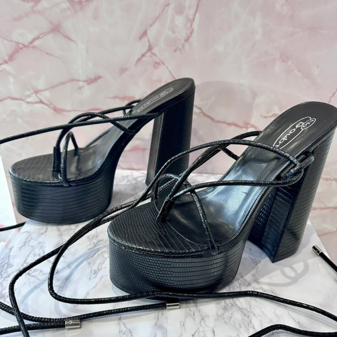 Black lizard-textured platform heels with wraparound straps and block heel, laid on marble background for elegant fashion display