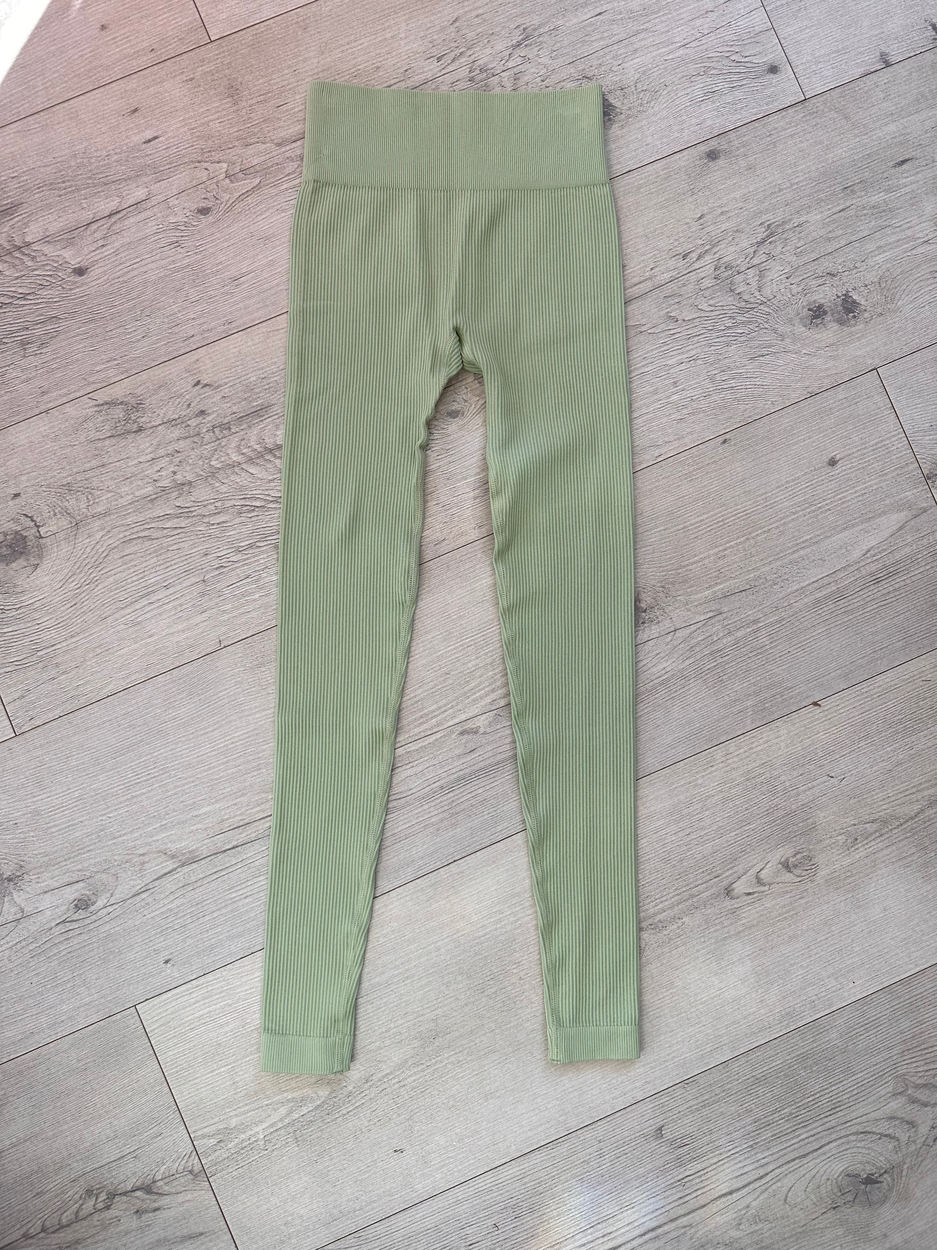 Flat lay of sage green ribbed leggings with a straight high-rise waistband, neatly displayed on a light wooden floor in natural lighting