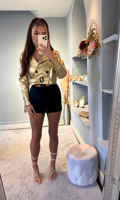 Woman modeling a gold belted cropped jacket with a black mini skirt and rhinestone lace-up heels — stylish and trendy party outfit for women