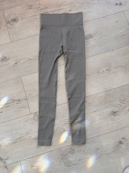 Flat lay of grey ribbed high-waisted leggings with V-shaped contour waistband, placed on a light wood floor with rainbow light reflections
