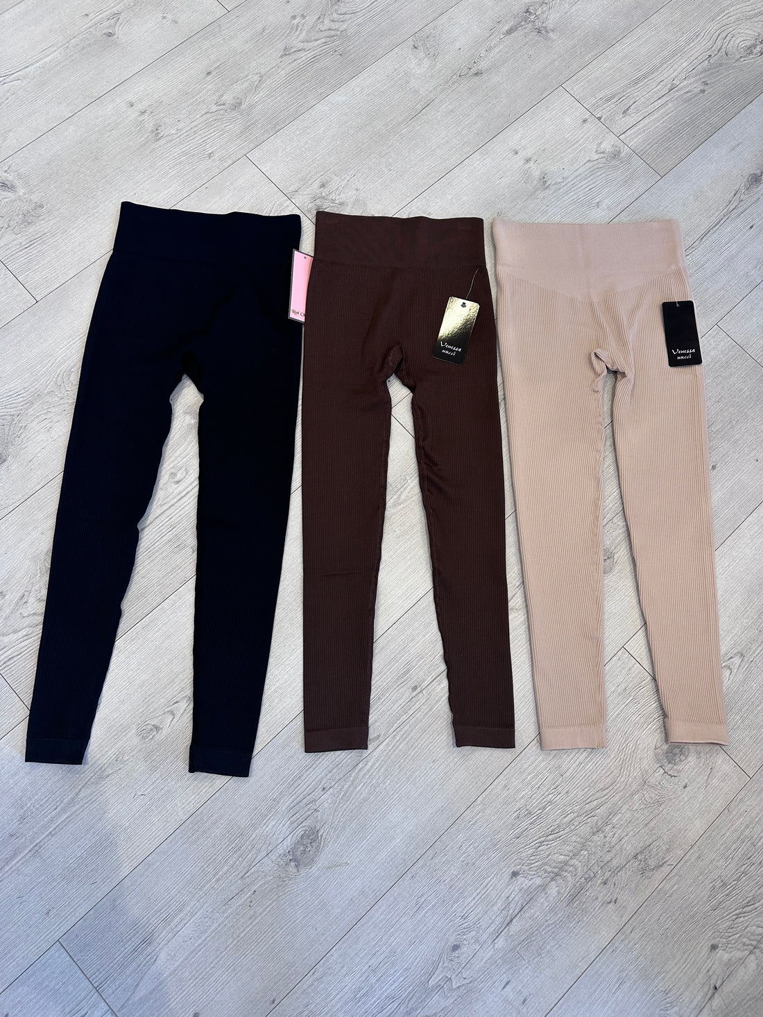 Set of three ribbed high-waist leggings in black, chocolate brown, and beige, laid flat on wooden flooring for a neutral fashion display