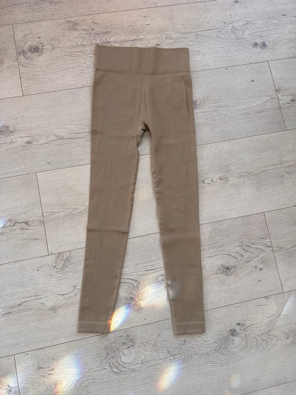 Flat lay of taupe ribbed high-waisted leggings with contour waistband, displayed on a light wood floor with soft rainbow light reflections